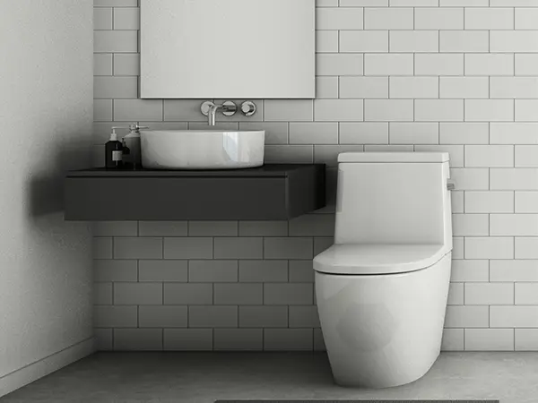 A simple toilet close to a dark countertop with a white vessel sink