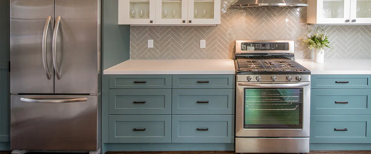 Blue base cabinets with white superior cabinets in a kitchen with a range and tile backsplash
