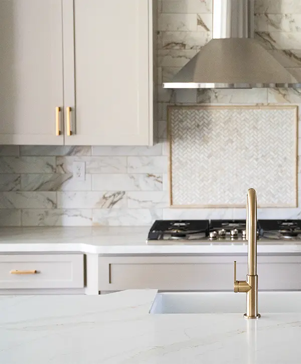 A quartz kitchen countertop with a golden faucet, undermount sink, kitchen range, and modern cabinets