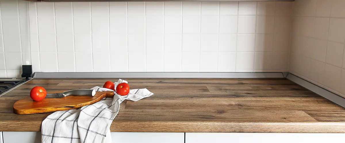 A laminate countertop with a cutting board and two tomatoes