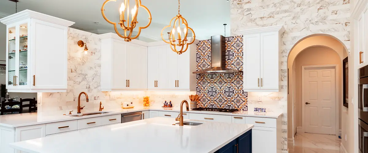 Luxurious kitchen with a large white island, gold fixtures, and decorative tile backsplash