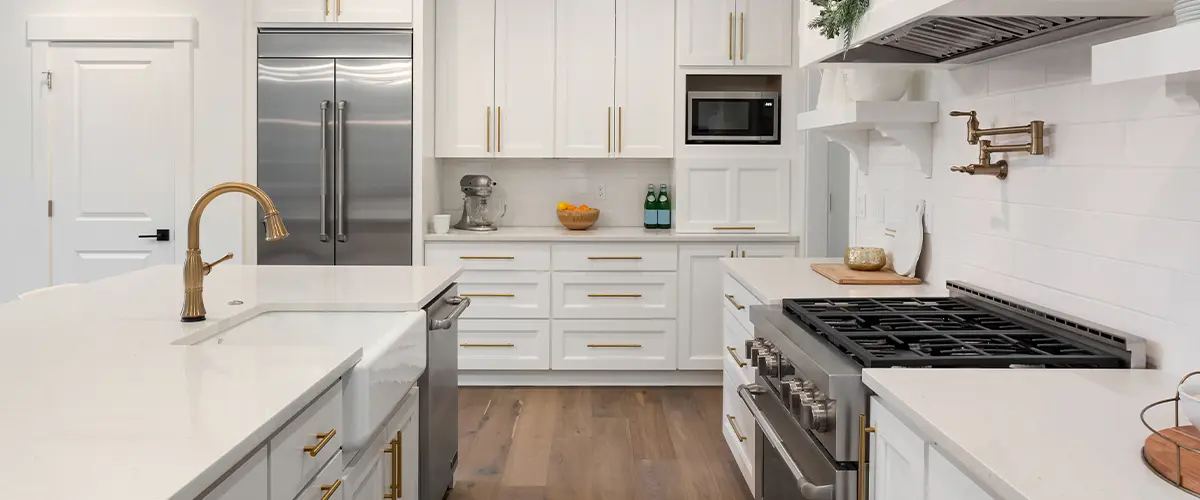 Modern white kitchen with gold accents and large island, featuring stainless steel appliances and farmhouse sink.