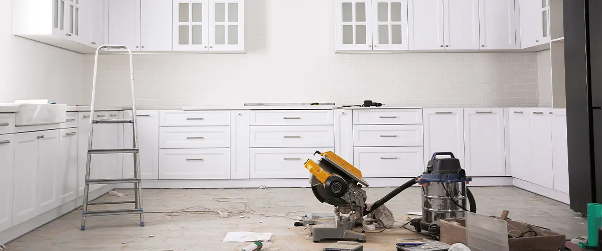 Spacious kitchen under renovation with white cabinets and modern lighting, tools and materials scattered on the floor.