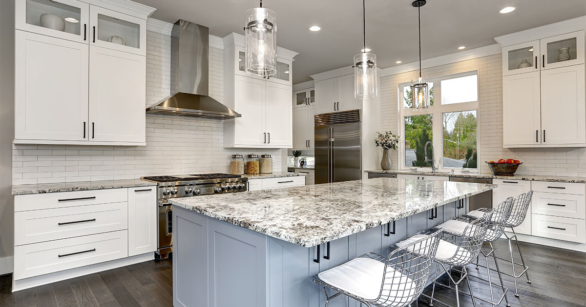 Modern white kitchen with granite countertops, stainless steel appliances, and a large island with pendant lighting.
