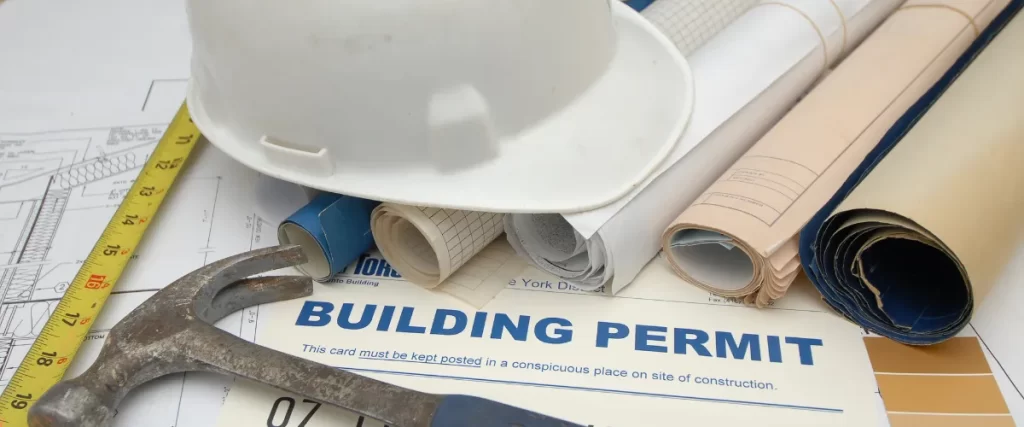 Building permit documents with rolled-up blueprints and a white hard hat on top.