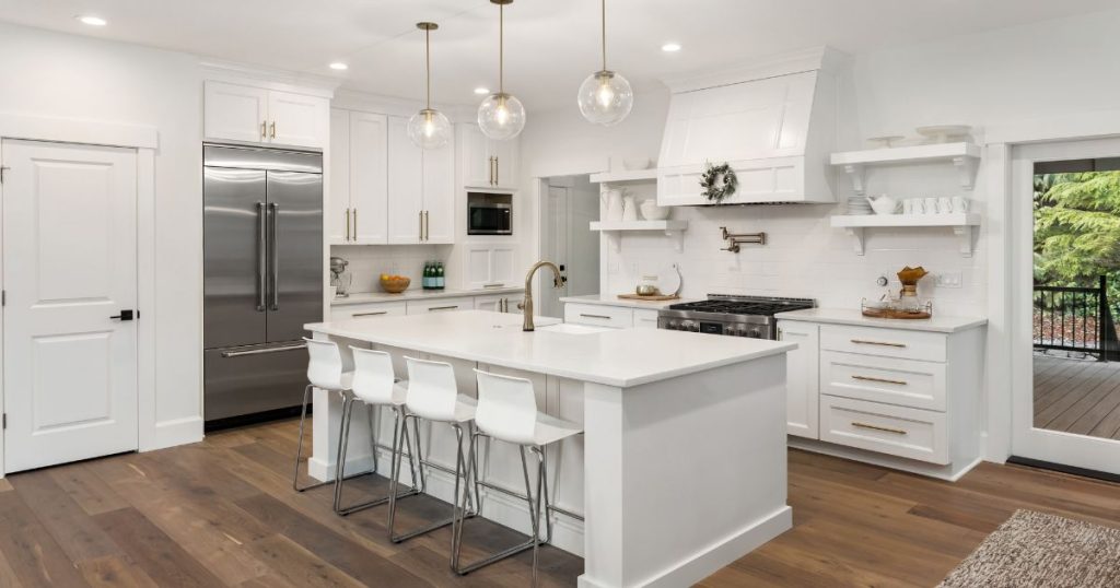 Elegant white kitchen with a spacious island, bar stools, and stylish pendant lights.