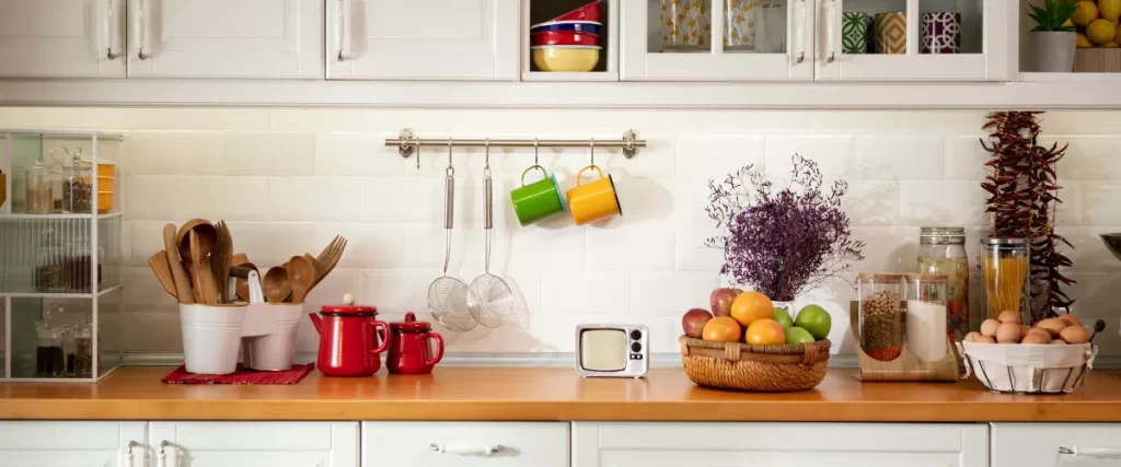 Close-up of a white kitchen countertop with hanging colorful mugs, a cutting board, and kitchen essentials.