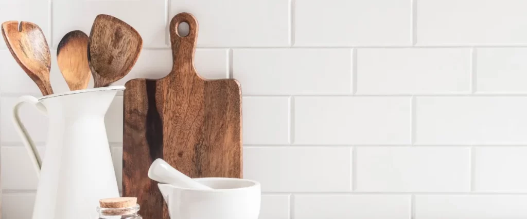 White subway tile backsplash with a wooden cutting board and a white ceramic cup.