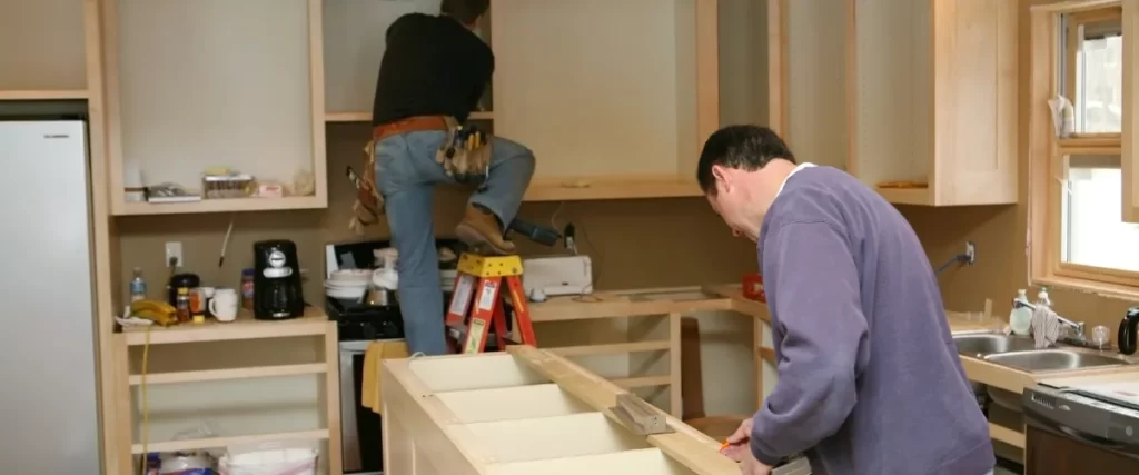 Two carpenters assembling wooden cabinets in a workshop.