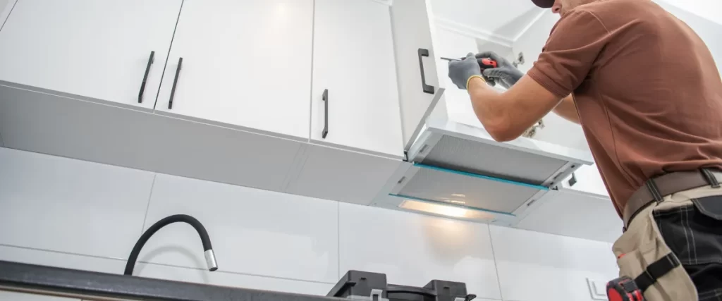 Worker installing a white kitchen cabinet using a power drill.