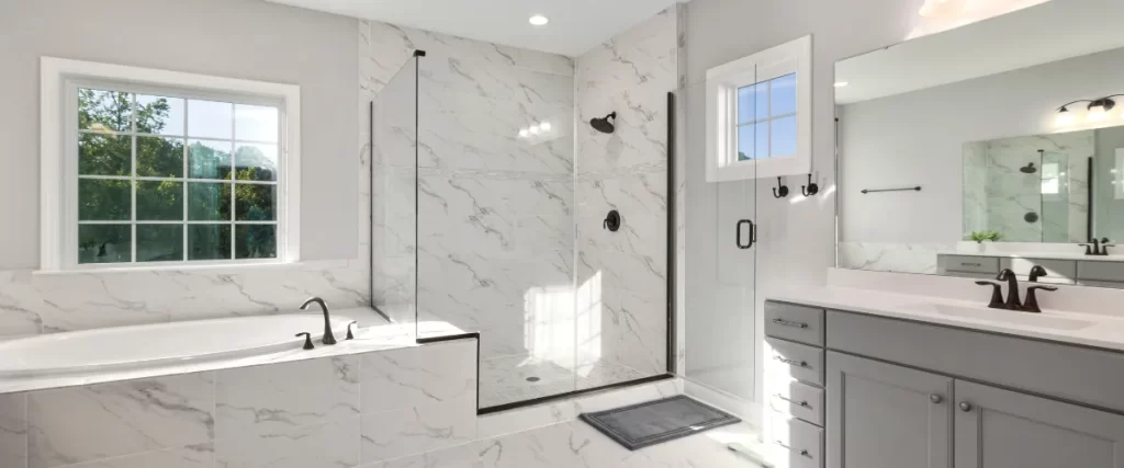 Spacious walk-in shower with white marble tiles, black fixtures, and a glass partition.