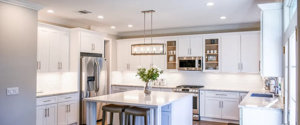 Modern white kitchen with a large island, pendant lighting, and stainless steel appliances.