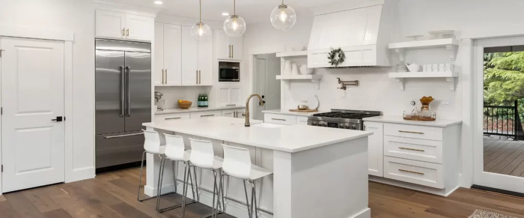 Modern white kitchen with a large island, bar stools, and pendant lighting.