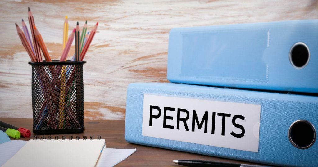 Blue binders labeled permits on a desk with office supplies