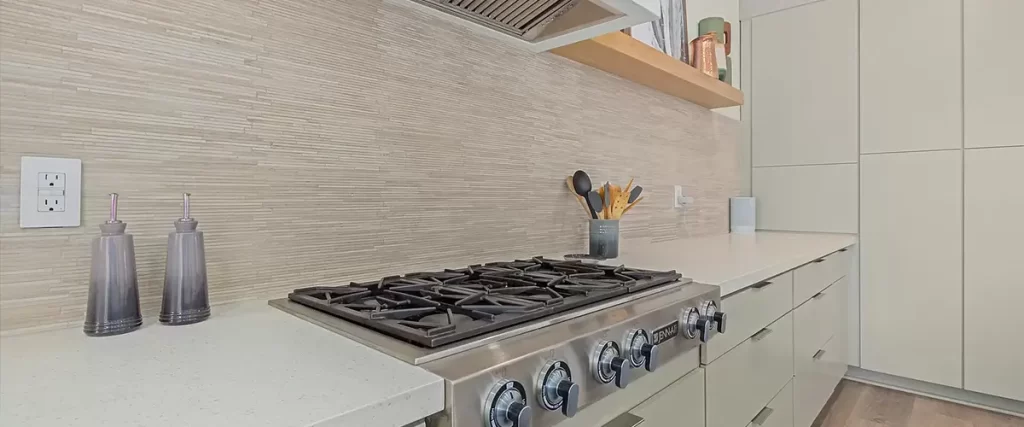 Modern kitchen with stainless steel gas cooktop, sleek vent hood, and light textured backsplash for a luxury remodel