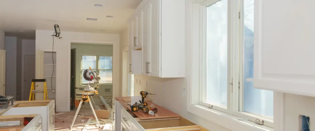 A bright, modern kitchen with white cabinets and a wooden countertop, tools visible suggesting ongoing renovation.