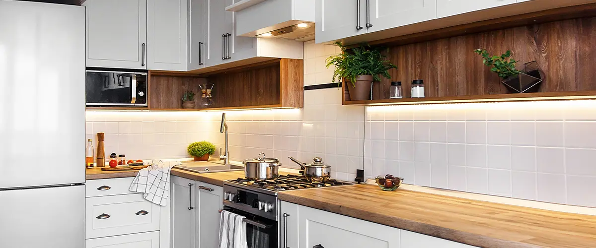 Modern L-shaped kitchen with wood countertops, white cabinets, under-cabinet lighting, and potted plants