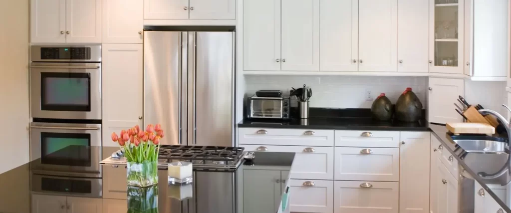 A classic white kitchen with shaker cabinets, black countertops, and built-in stainless steel appliances, including double wall ovens and a refrigerator.