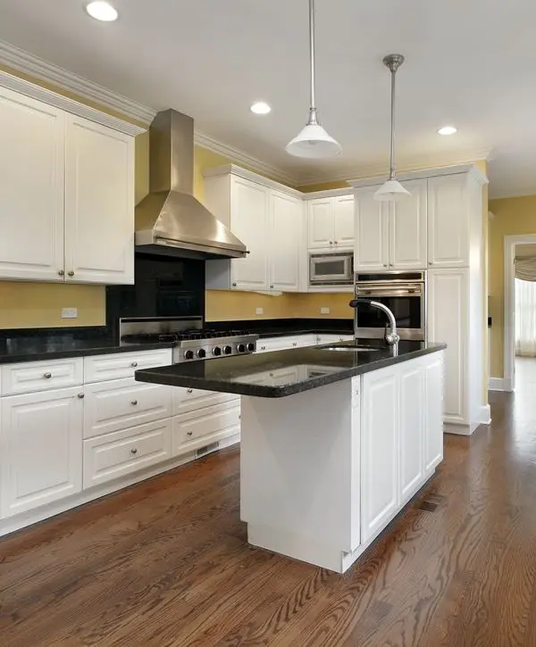 A luxurious Mill Creek, WA kitchen remodel featuring a bold navy blue island with a white quartz countertop, contrasting white perimeter cabinets, a decorative patterned tile backsplash, gold hardware and light fixtures, and stainless steel appliances.