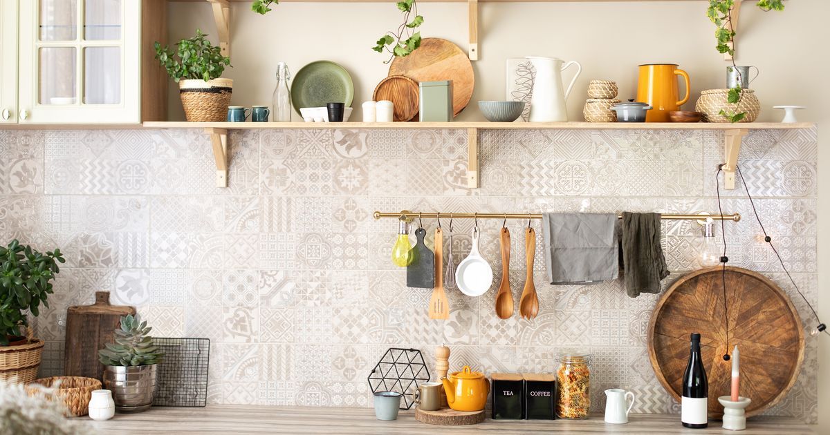 Modern kitchen with open wooden shelving above a patterned tile backsplash, showing organized plates, pitchers, and kitchen tools hanging on a brass rail