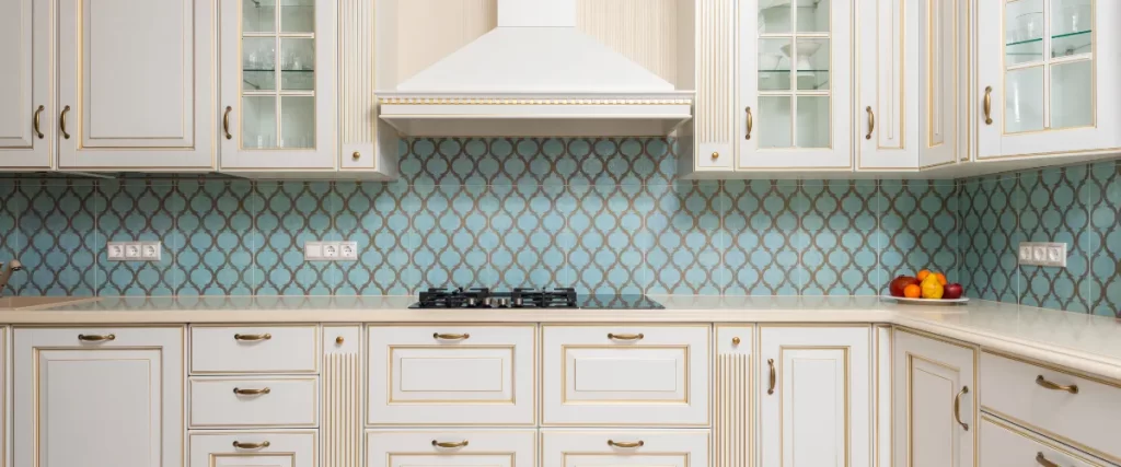 Ornate white kitchen cabinetry with subtle gold trim and glass fronts, set against a unique blue and white patterned arabesque tile backsplash