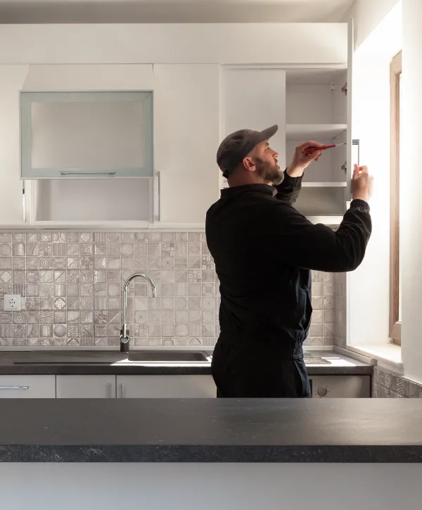 A man is performing maintenance or installation work on new kitchen cabinets