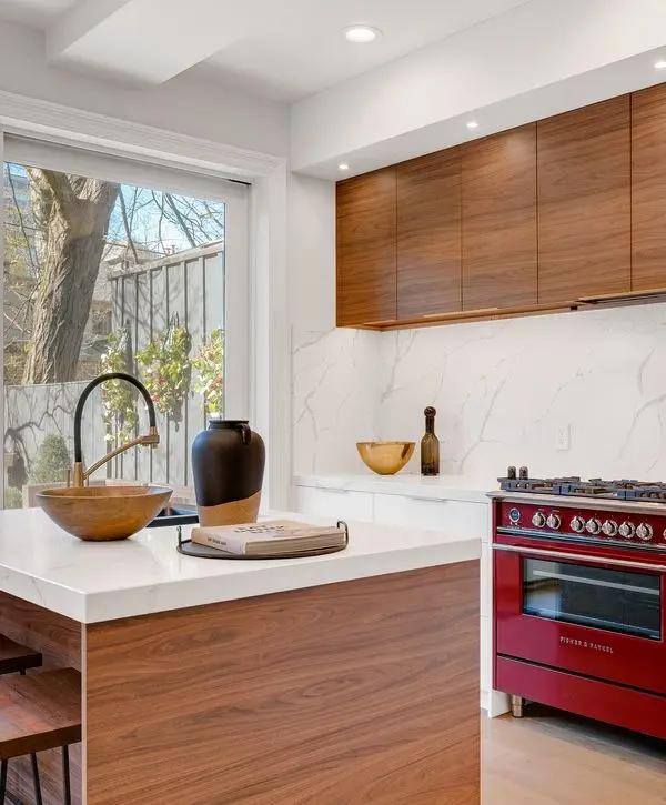 A modern kitchen featuring warm walnut wood cabinetry, a white marble backsplash, and a striking red Fisher and Paykel gas range in a Lake Forest Park, WA home.