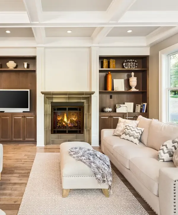 A beautifully renovated living room in Burien, WA, featuring a stone-clad gas fireplace, custom dark wood built-in bookshelves, coffered ceilings, and a neutral-toned sectional sofa.