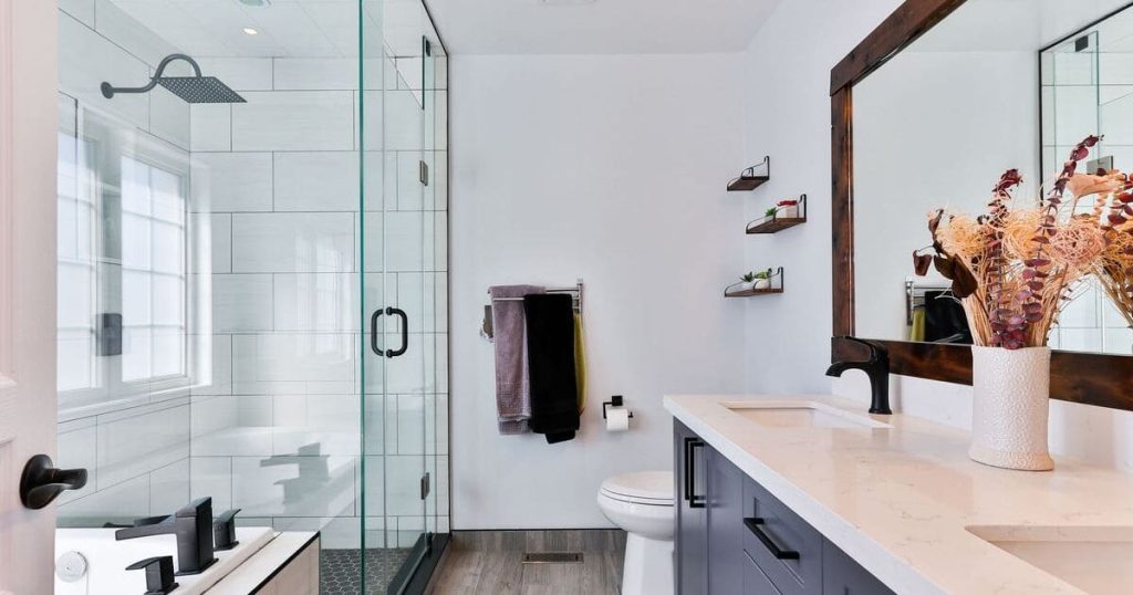 A bright modern bathroom featuring a spacious walk-in shower with a glass enclosure, white subway tiles, a navy blue vanity with a white countertop, and a dark wood-framed mirror.
