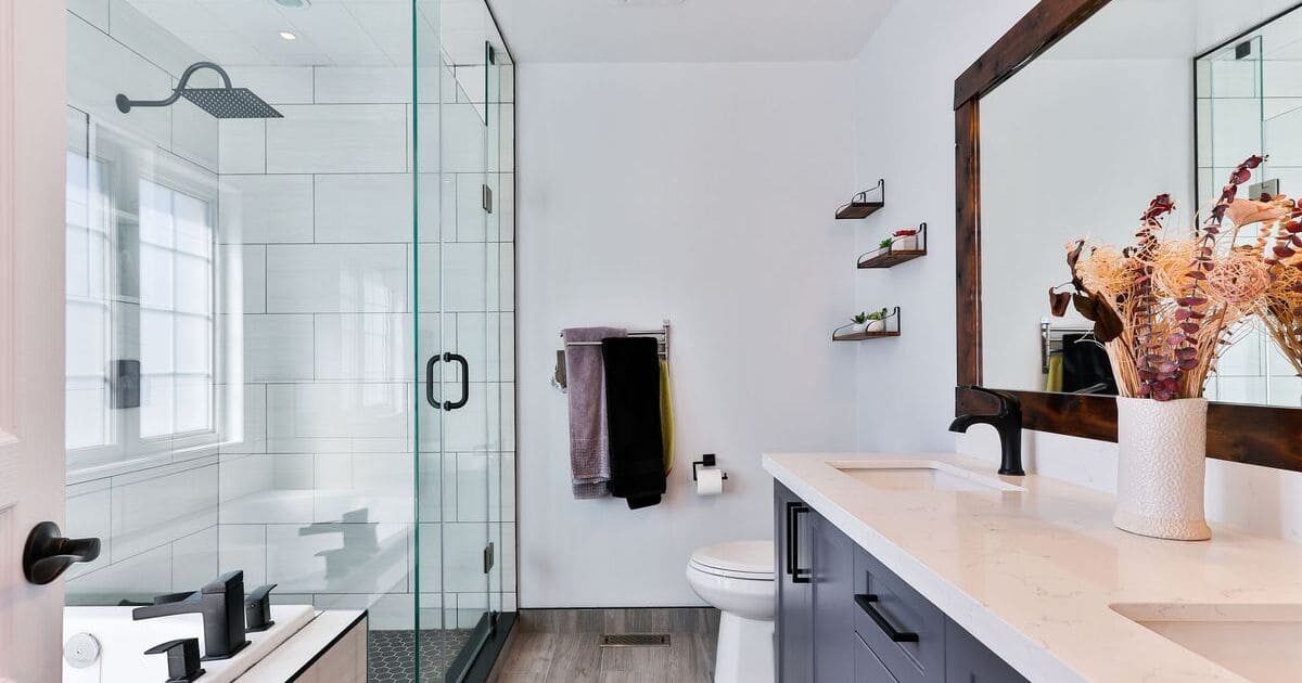A bright modern bathroom featuring a spacious walk-in shower with a glass enclosure, white subway tiles, a navy blue vanity with a white countertop, and a dark wood-framed mirror.