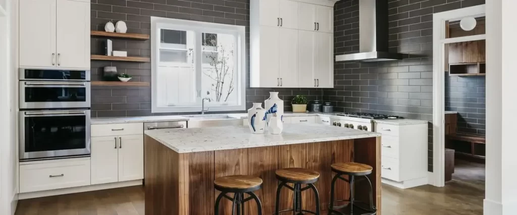 A modern kitchen featuring white upper cabinets, a dark grey subway tile backsplash, and a rich walnut wood island with marble countertop and three industrial stools.