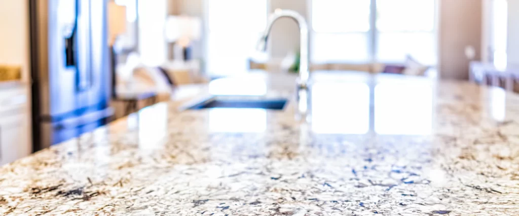 A wide-angle, blurred background shot focusing on the textured surface of a polished granite kitchen island countertop with a sleek chrome faucet.