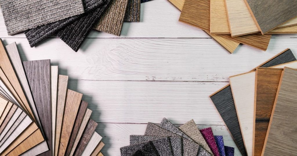 A top-down view of various flooring samples including carpet, wood, and vinyl planks arranged on a white wood surface to find the best flooring for Arizona homes.