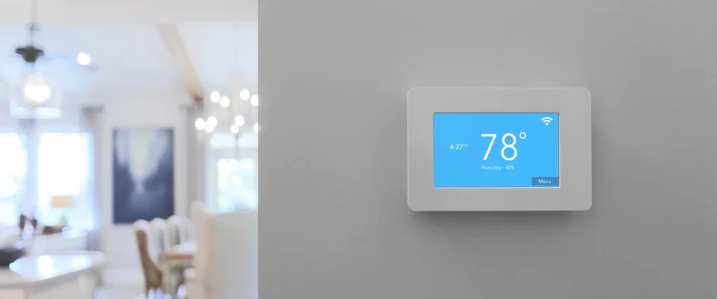 A sleek digital smart thermostat mounted on a white wall showing temperature control settings.
