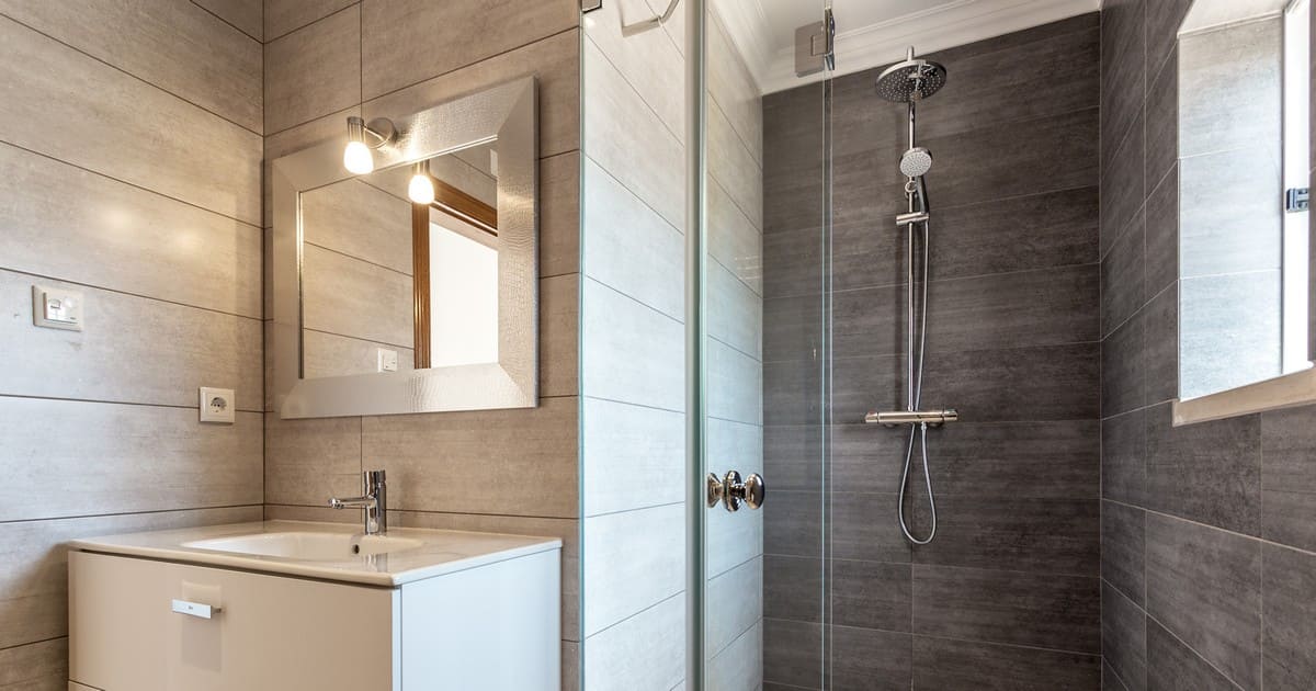 A modern bathroom featuring a grey tiled glass shower enclosure and a white vanity, showcasing the Best Bathroom Materials for Extreme Phoenix Heat.