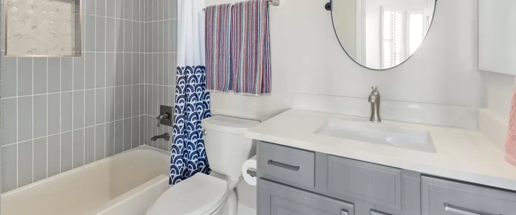 Modern gray bathroom remodel with tiled tub shower, custom vanity, and round mirror
